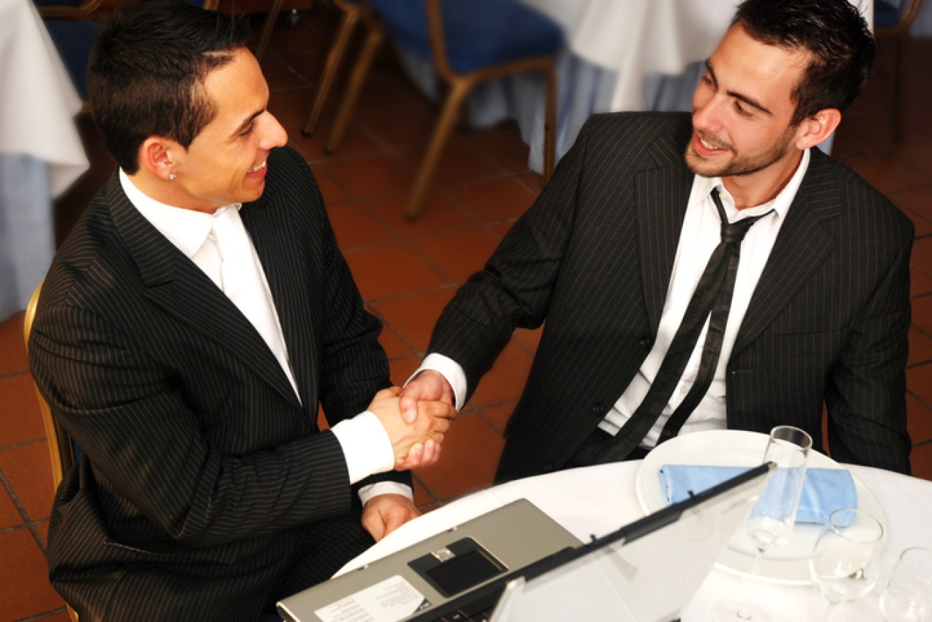 Two young businesmen shaking hands at a restaurant.