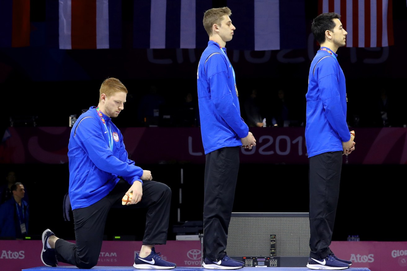 Gold medalist Race Imboden takes a knee while the US national anthem is played in Lima. 