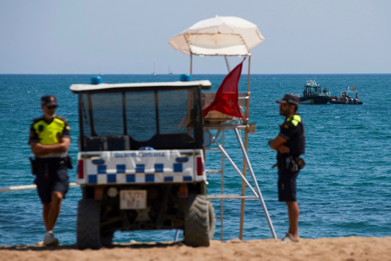Police stand guard on the sand at Sant Sebastia while, in the water, divers recover the suspected bomb.