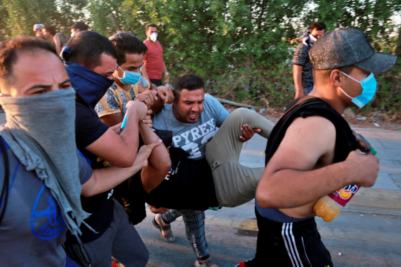 Protesters carry a wounded comrade to safety amid a hail of bullets in havoc-stricken Baghdad.