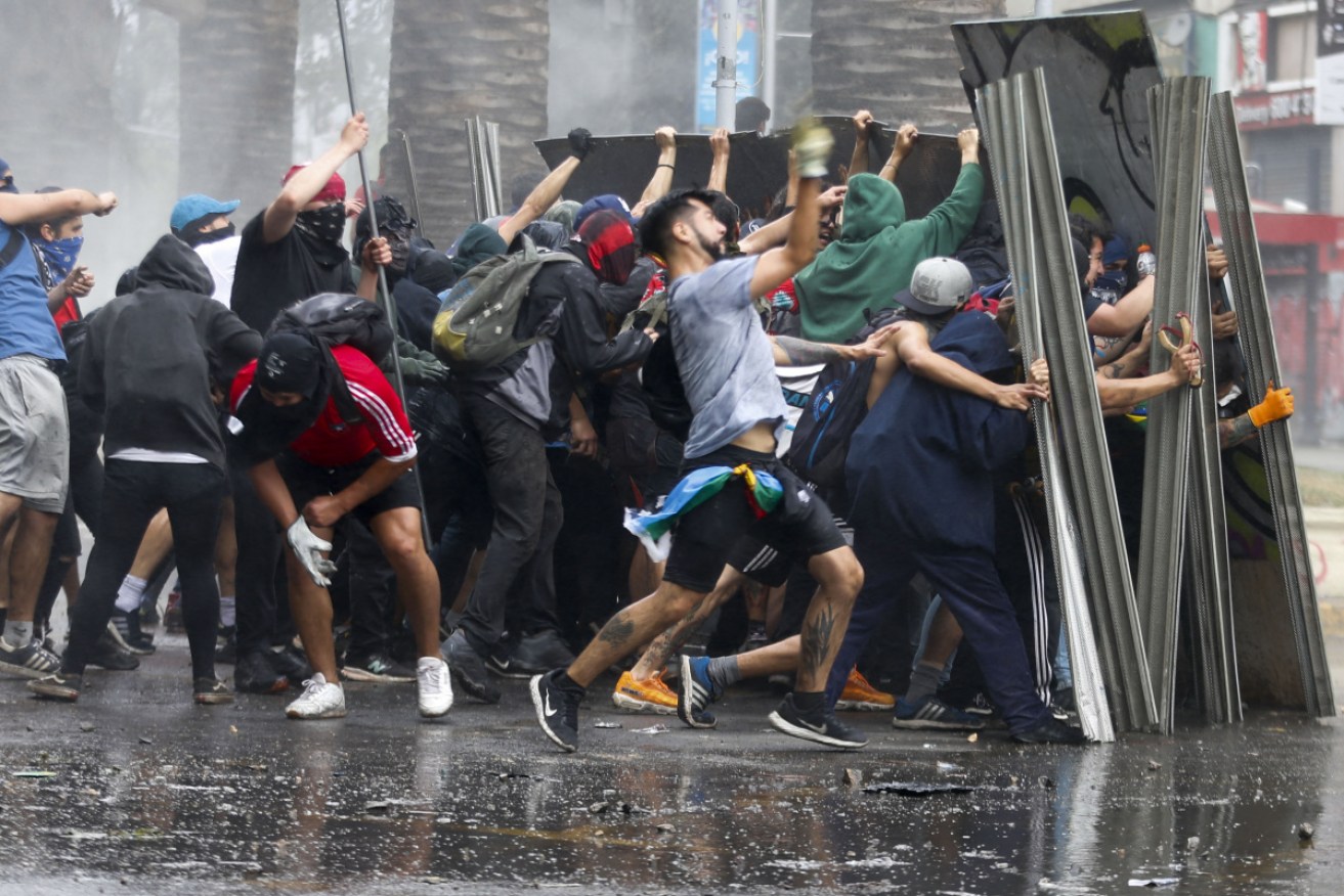 Anti-government protesters take cover against police during a riot in Chile on October 24.