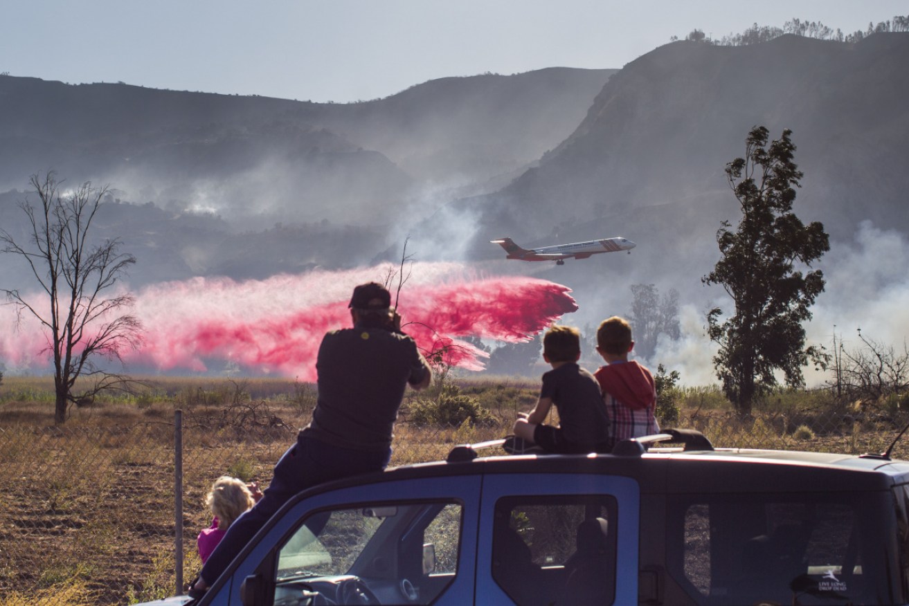 A family watches an Air Tanker dropping fire retardant over lines while helping to fight the Maria fire, in Santa Paula, Ventura County, in California. 