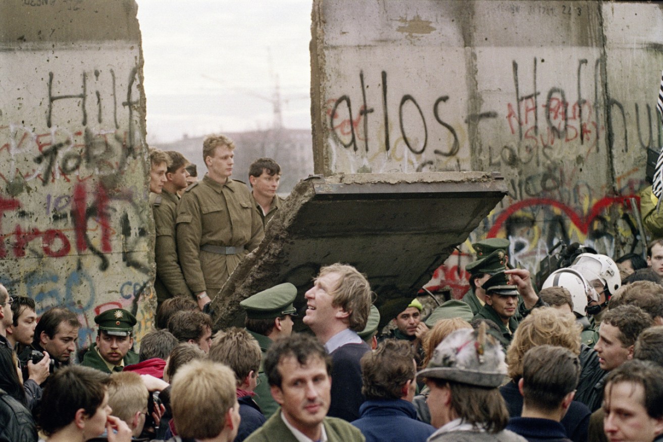 West Berliners crowd in front of the Berlin Wall as they watch East German border guards demolishing a section of the wall.