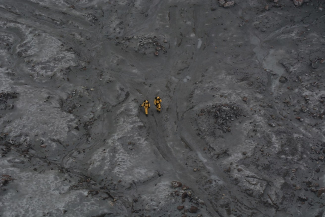 Rescuers in protective hazmat suits brave the lethal conditions on New Zealand's White Island to retrieve bodies. 