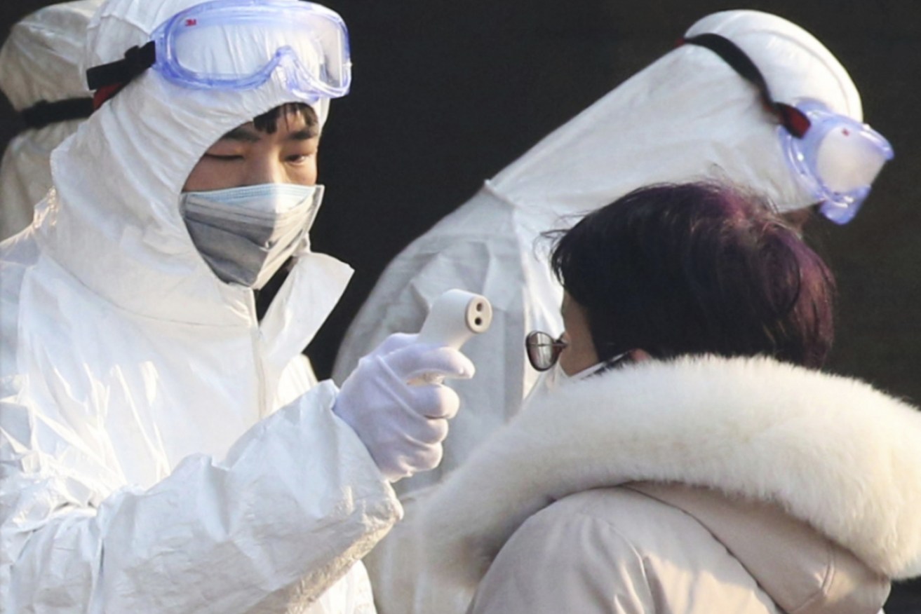 Security staff clad in protective clothing check the body temperature of passengers at the entrance of a subway station in Beijing on Saturday.