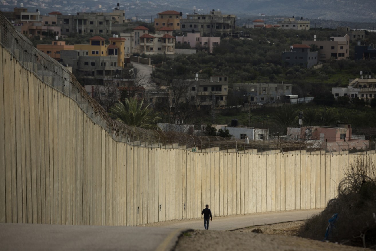 A man walks near the Israeli West Bank barrier as the Palestinian village Naslat Isa is seen on the other side of the barrier.