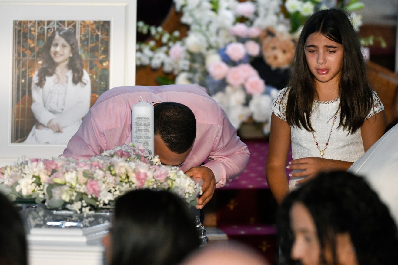 Danny Adballah (left) kisses one of his children's coffins, while his daughter stands besides him.