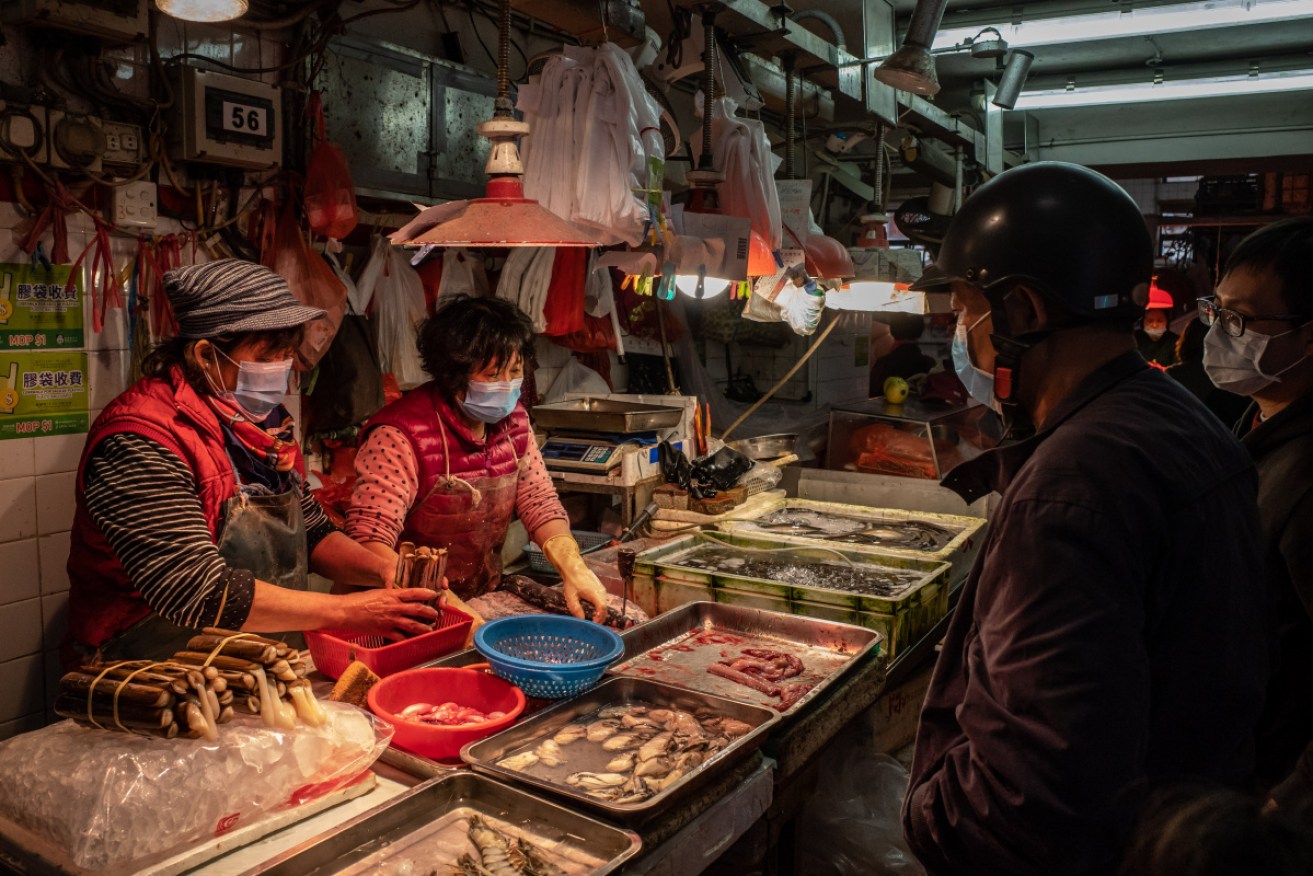 Masked vendors slicing fresh meat for customers at a wet market in Macau, China.
