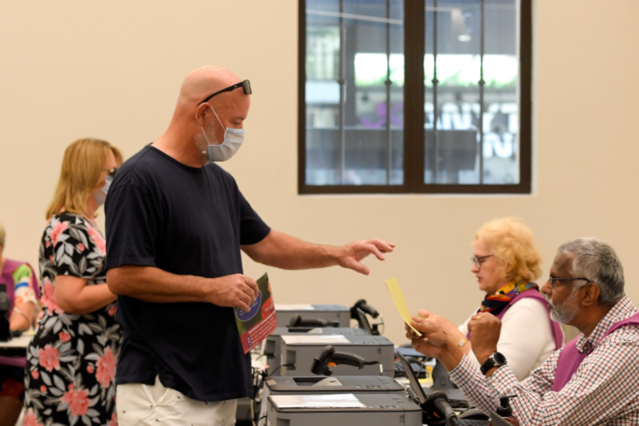 A Queensland voter prepares to cast his ballot from behind a virus mask.