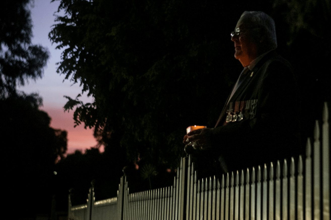 Candle in hand, a serviceman marks Anzac Day in silence and locked-down isolation by his front fence. 