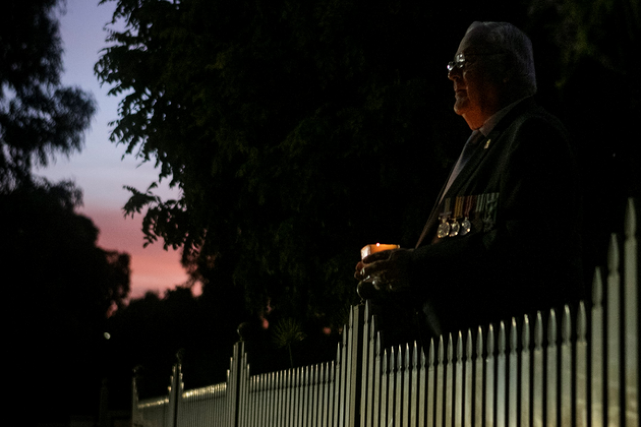 Candle in hand, a serviceman marks Anzac Day in silence and locked-down isolation by his front fence.