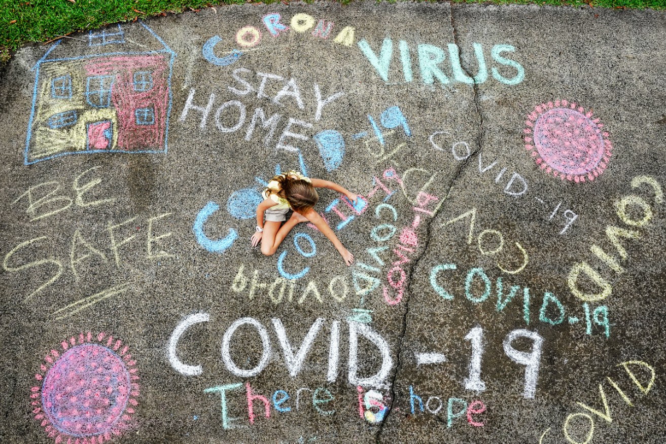 A Gold Coast girl writes in her driveway as students around Australia are let back to school at different times. 