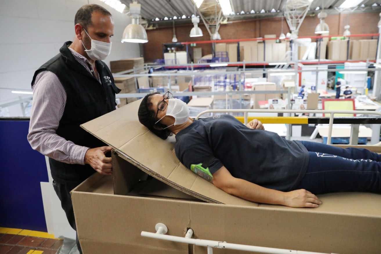 Rodolfo Gomez, left, shows how the hospital bed made of cardboard can serve patients with COVID-19.