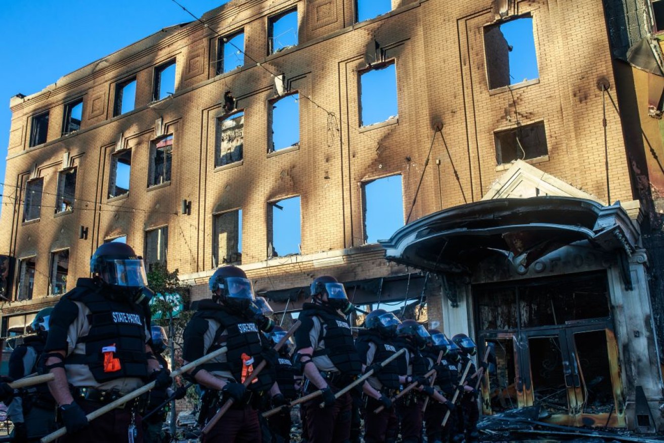 State Patrol Police officers block a road near a burnt building during a rally in Minneapolis.