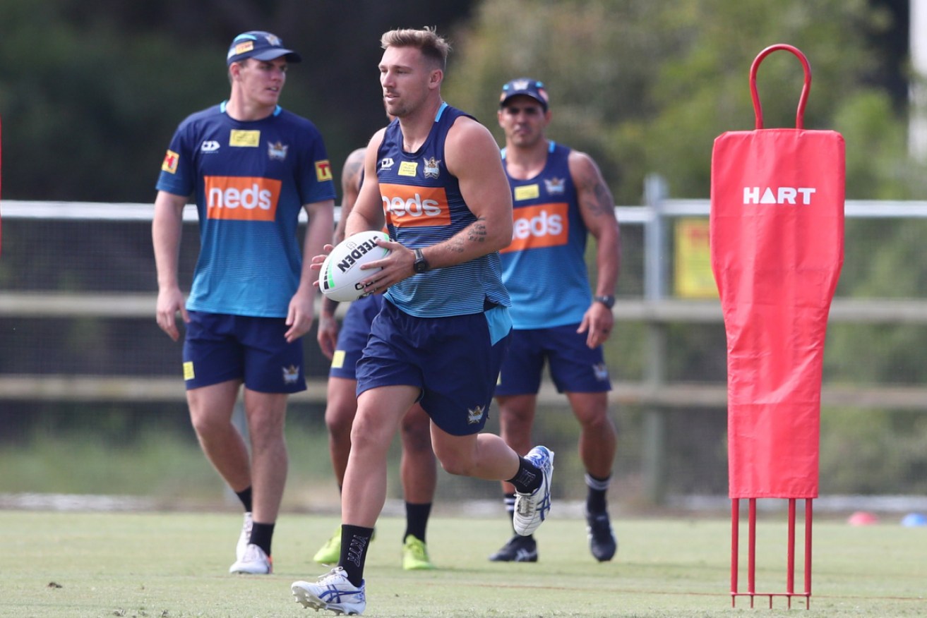 Gold Coast's Bryce Cartwright, centre, is being tackled over his anti-vaccination stance.