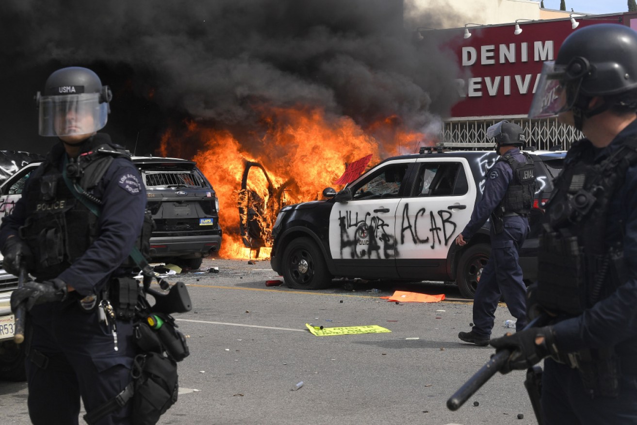 Los Angeles police officers watch a police car burn during a protest over the death of George Floyd.