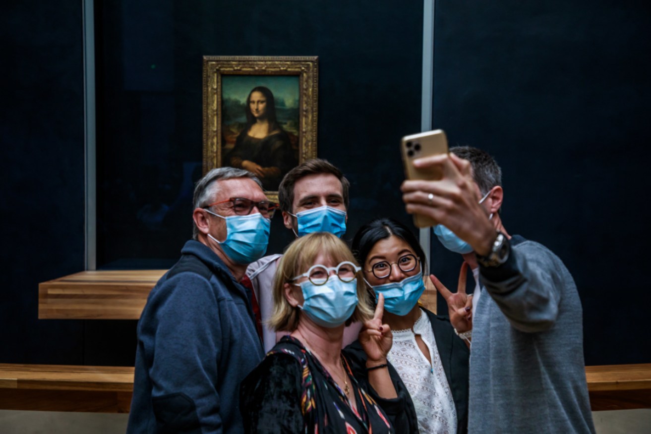 Mask-clad tourists pose for a selfie with the Mona Lisa.