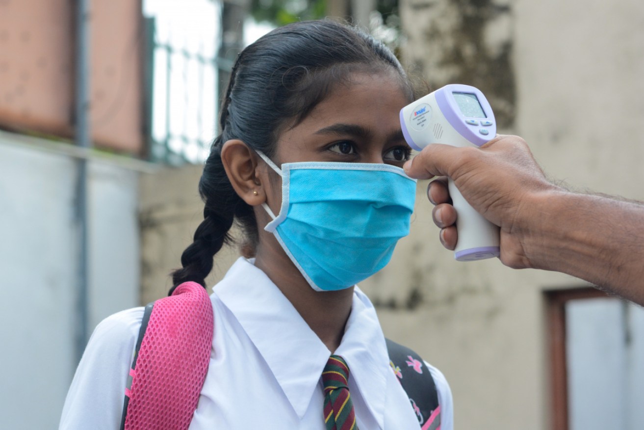 A student in Sri Lanka has her temperature taken on the way into school.
