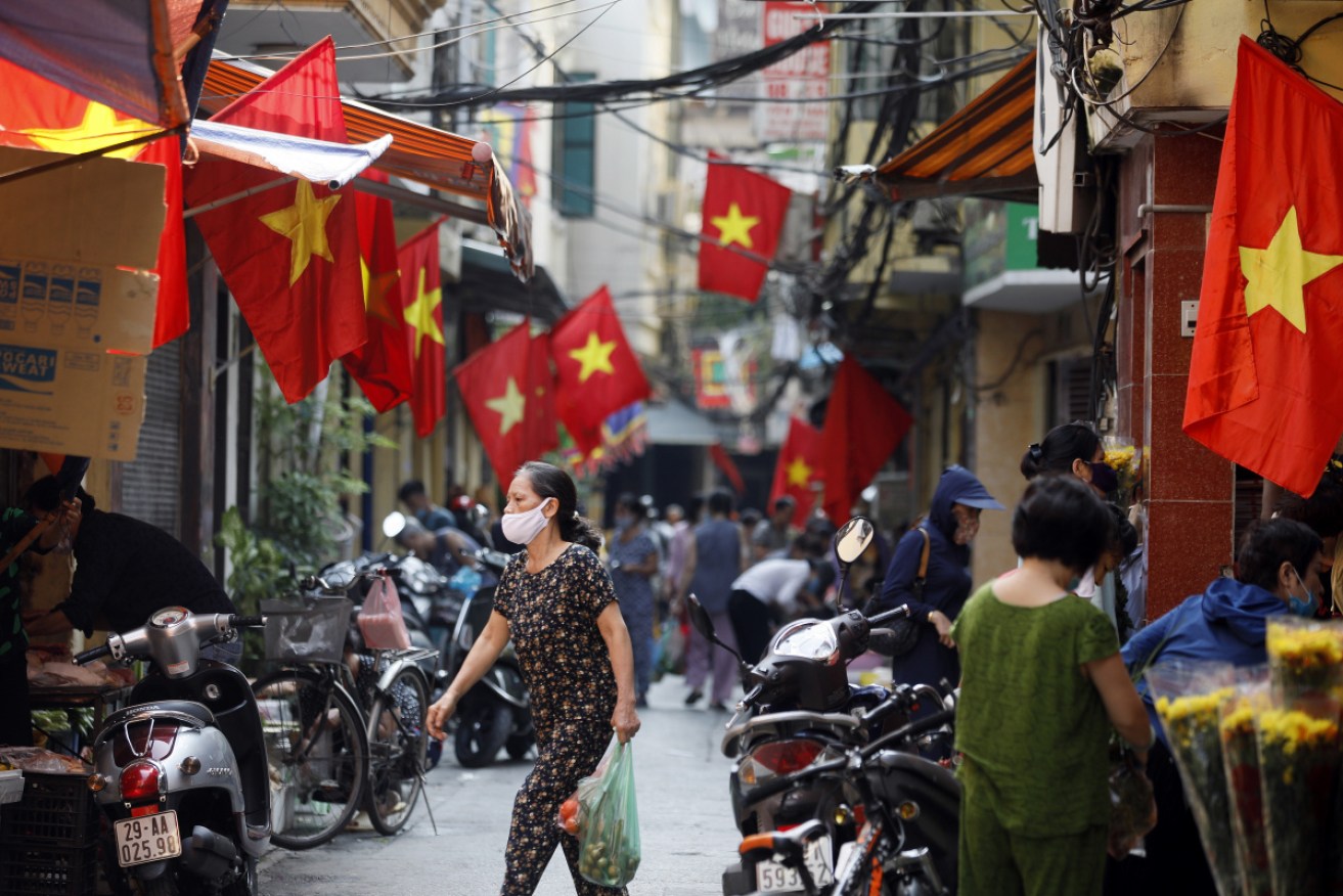 A woman walks under national flags at an alley in Hanoi, Vietnam as the nation ponders a travel bubble.