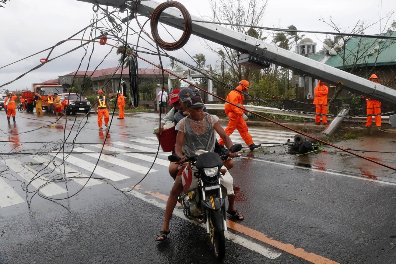 Villagers manoeuvre under a toppled electric post in the typhoon-hit town of Tigaon, Camarines Sur, Philippines.