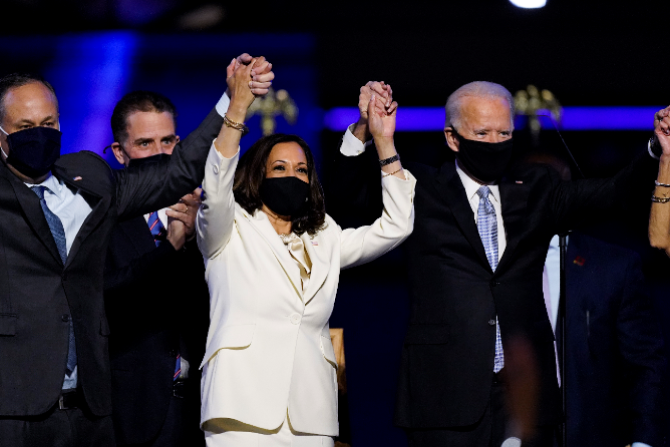 Joe Biden and Kamala Harris raise their hands in triumph amid the crowd's cheers.