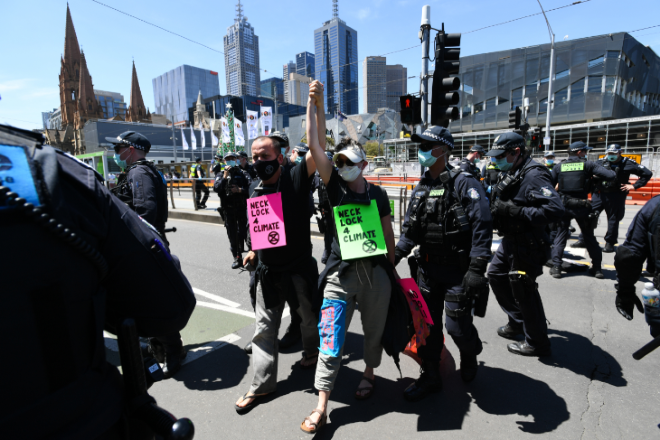 With bicycle locks around their necks, climate protesters are led are by police at Flinders Street Station.