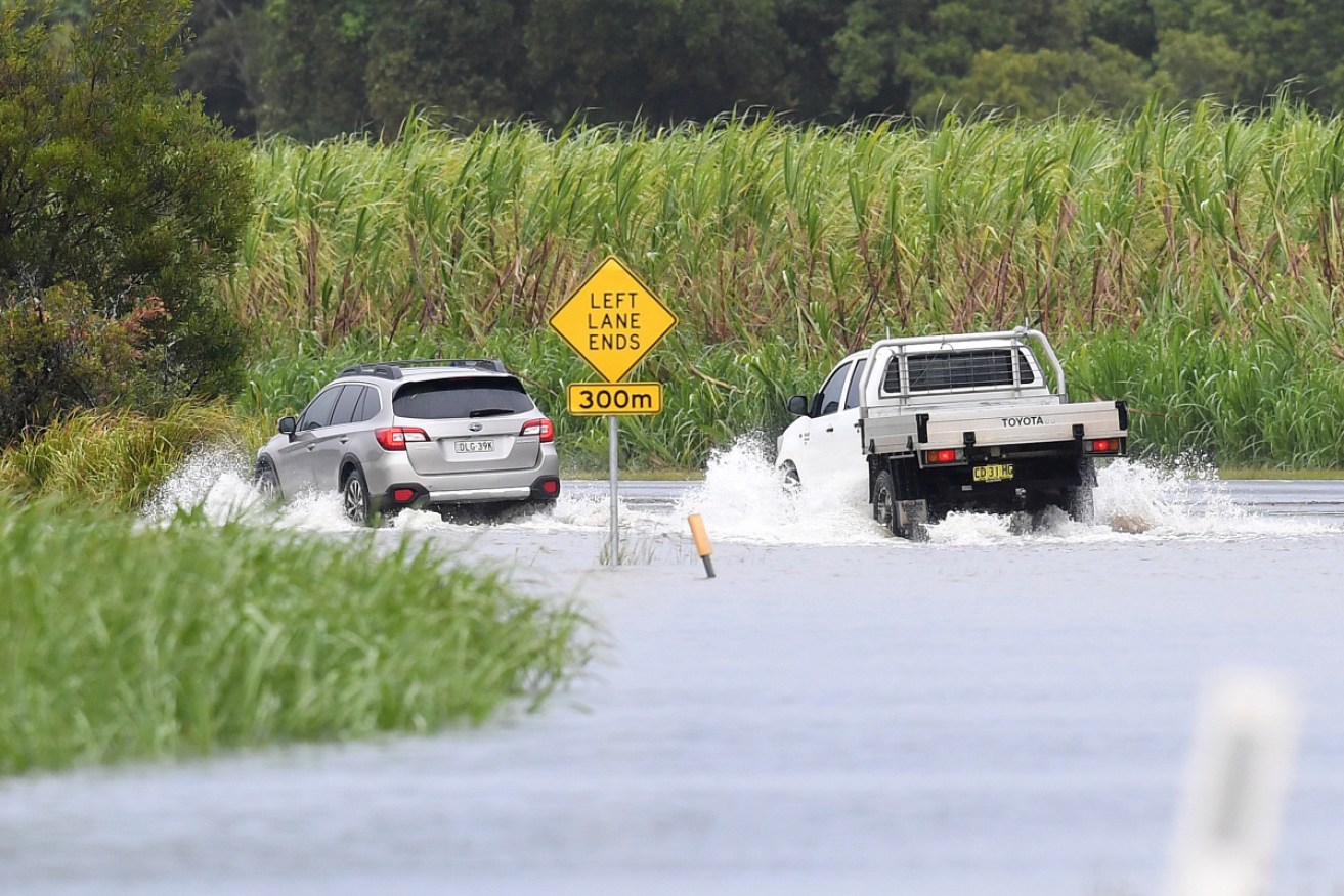 Cars drive through a flooded road at Tumbulgum, in the NSW northern rivers region.