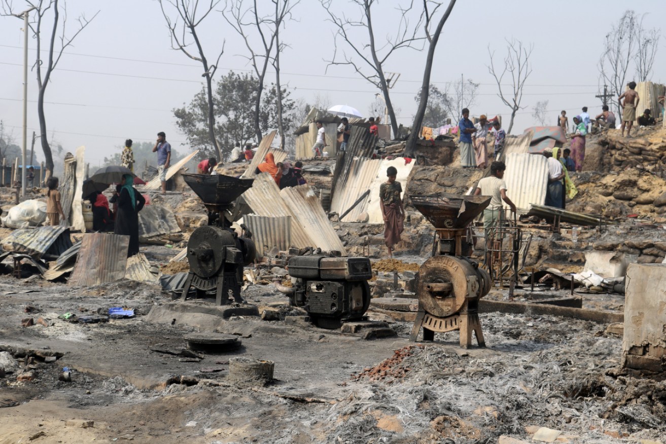 Rohingya refugees stand by remains of Monday's fire at a refugee camp at Balukhali, southern Bangladesh, on Tuesday.