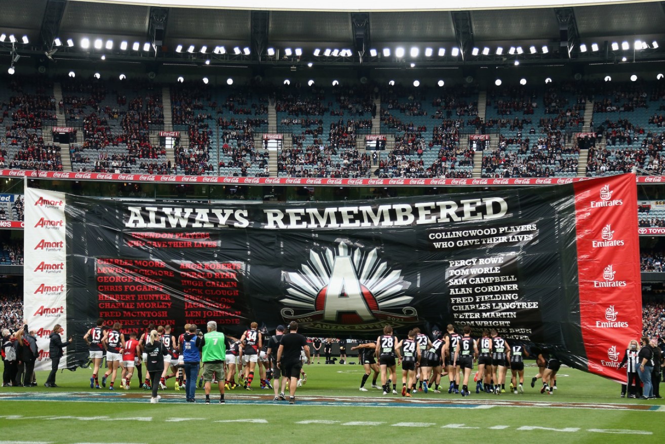 Essendon and Collingwood players run through the banner together before the AFL Anzac Day clash. 