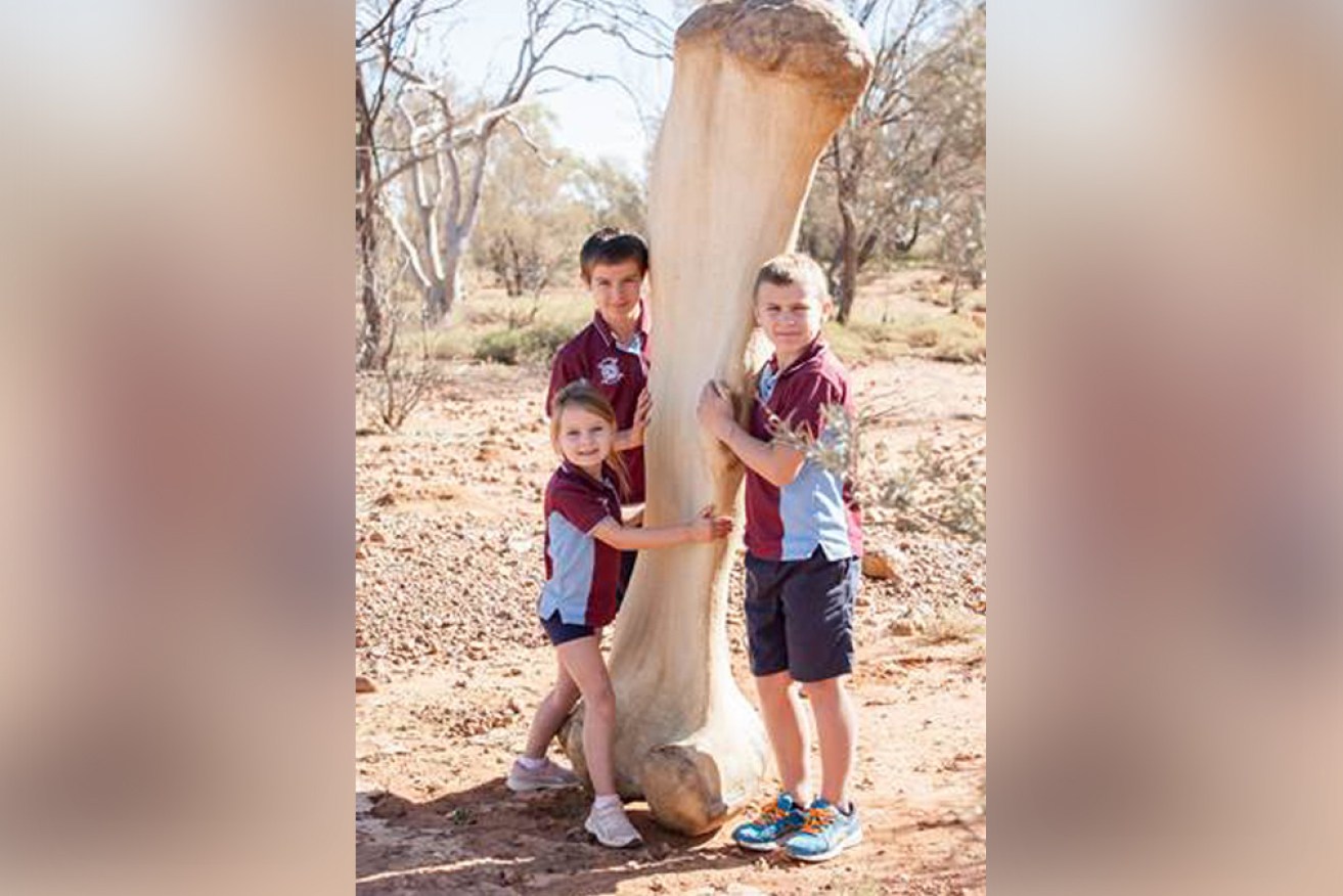 Children from Eromanga State School size up against a replica of Cooper's rear leg at the Eromanga Natural History Museum.