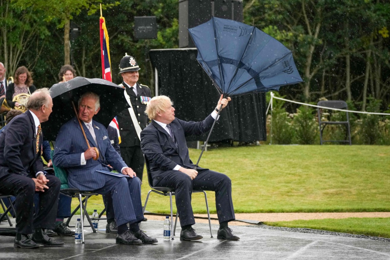 The British PM struggles with his wayward umbrella – to the amusement of a watching police officer.