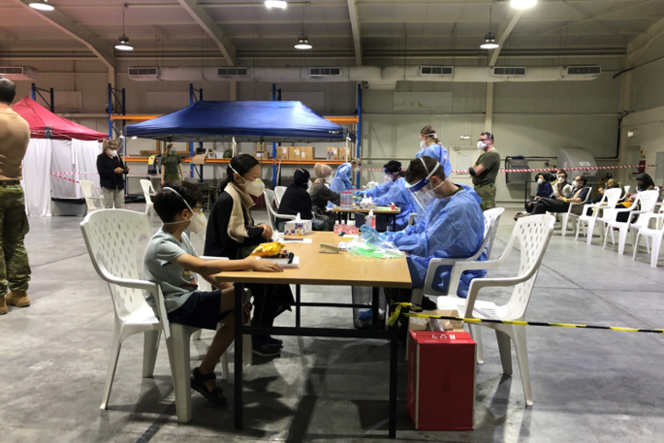 Australian Defence Force personnel in full PPE gear process two of the first evacuees from Kabul.