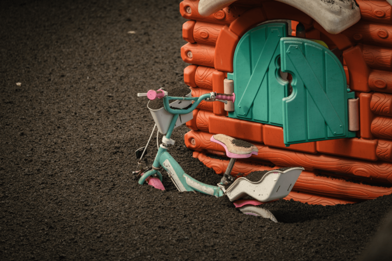 A child's bike and cubbyhouse lie half-buried in volcanic ash outside an evacuated La Palma home.