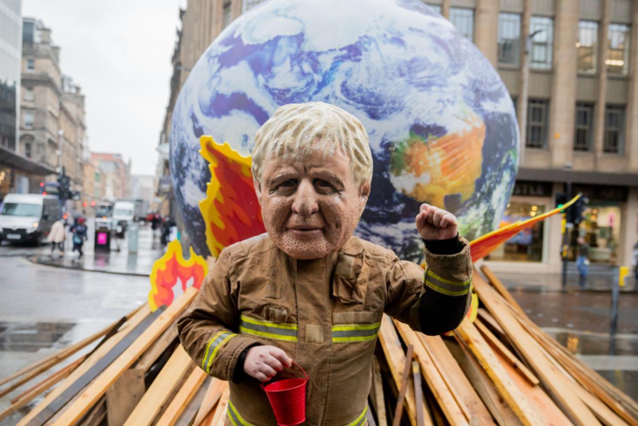 A protester in a Boris Johnson mask demands action as the earth burns on a climate bonfire.