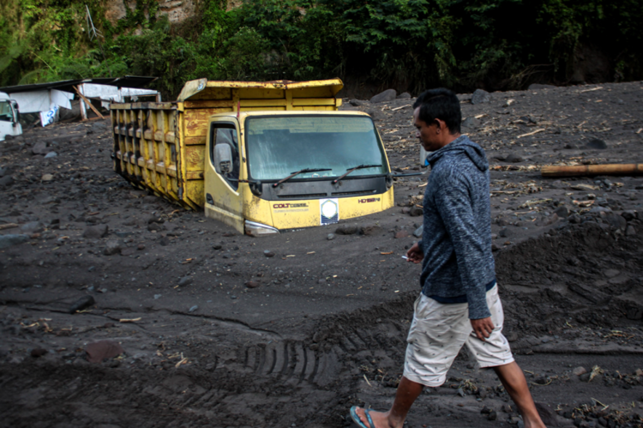 A villager picks his way through volcanic ash that came down so quickly it half-buried a tip-truck.