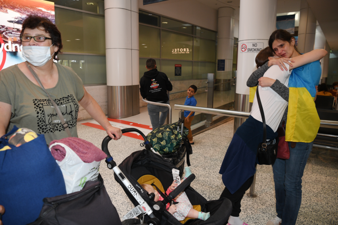 An emotional Olha Lyeskakova wears the Ukrainian flag as mum Olena, sister Iryna and little Oksana arrive safely in Sydney.<i>Photo: AAP</i>