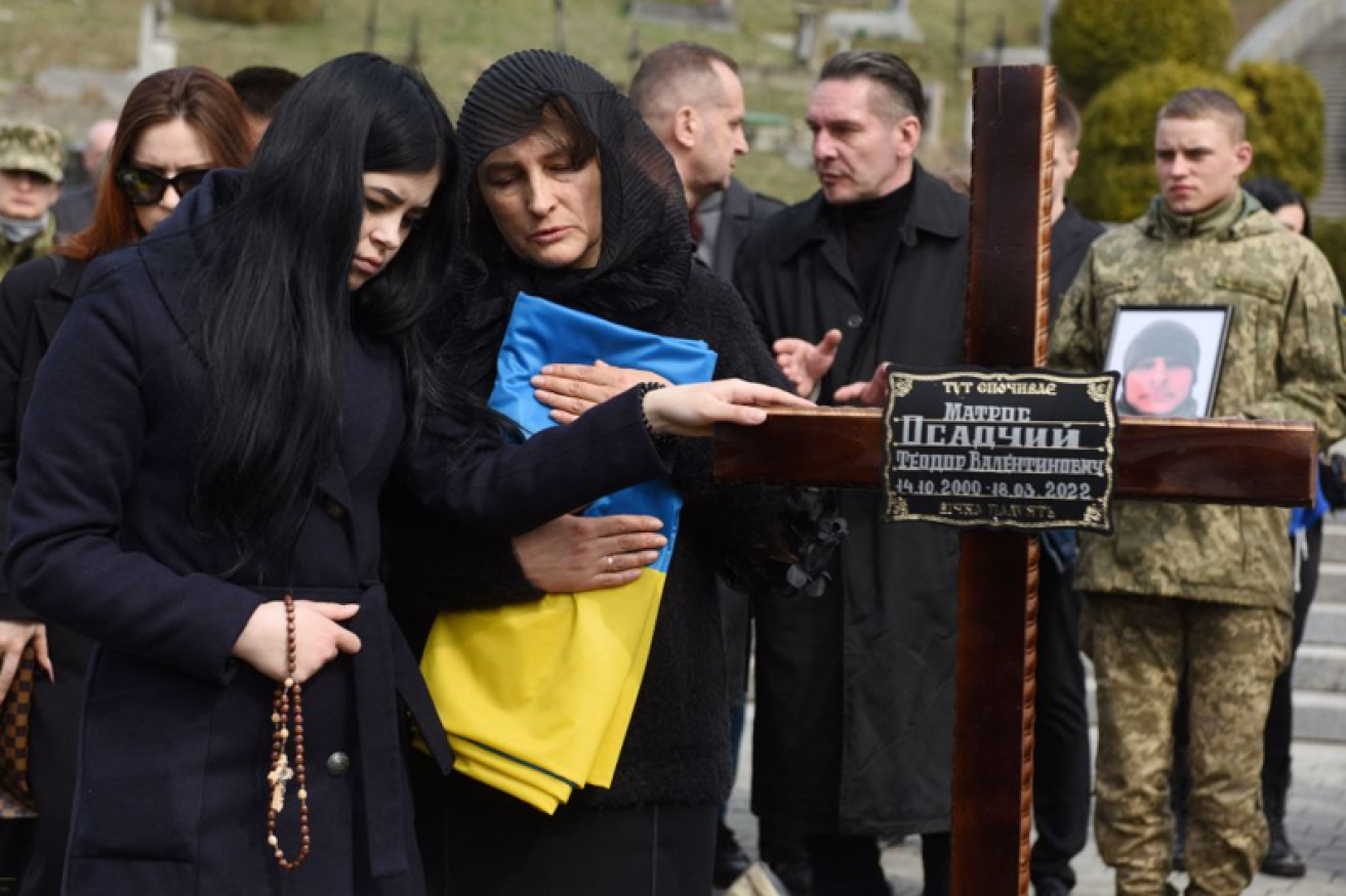 Ukrainian troops and relatives water the grave of a fallen comrade in a Kyiv cemetery. <i>Photo: Getty</i>