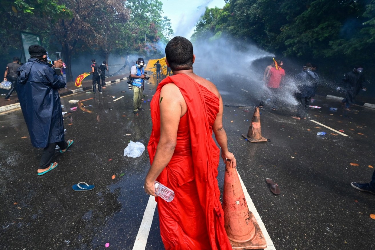 A Buddhist monk looks on a police use tear gas and a water canon to disperse protesting university students.
