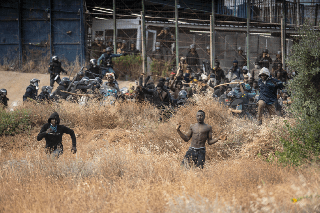 Africans seeking better lives in Spain burst through the Melilla border fence as police in the background try to stem the human tide. <i>Photo: AP</i>