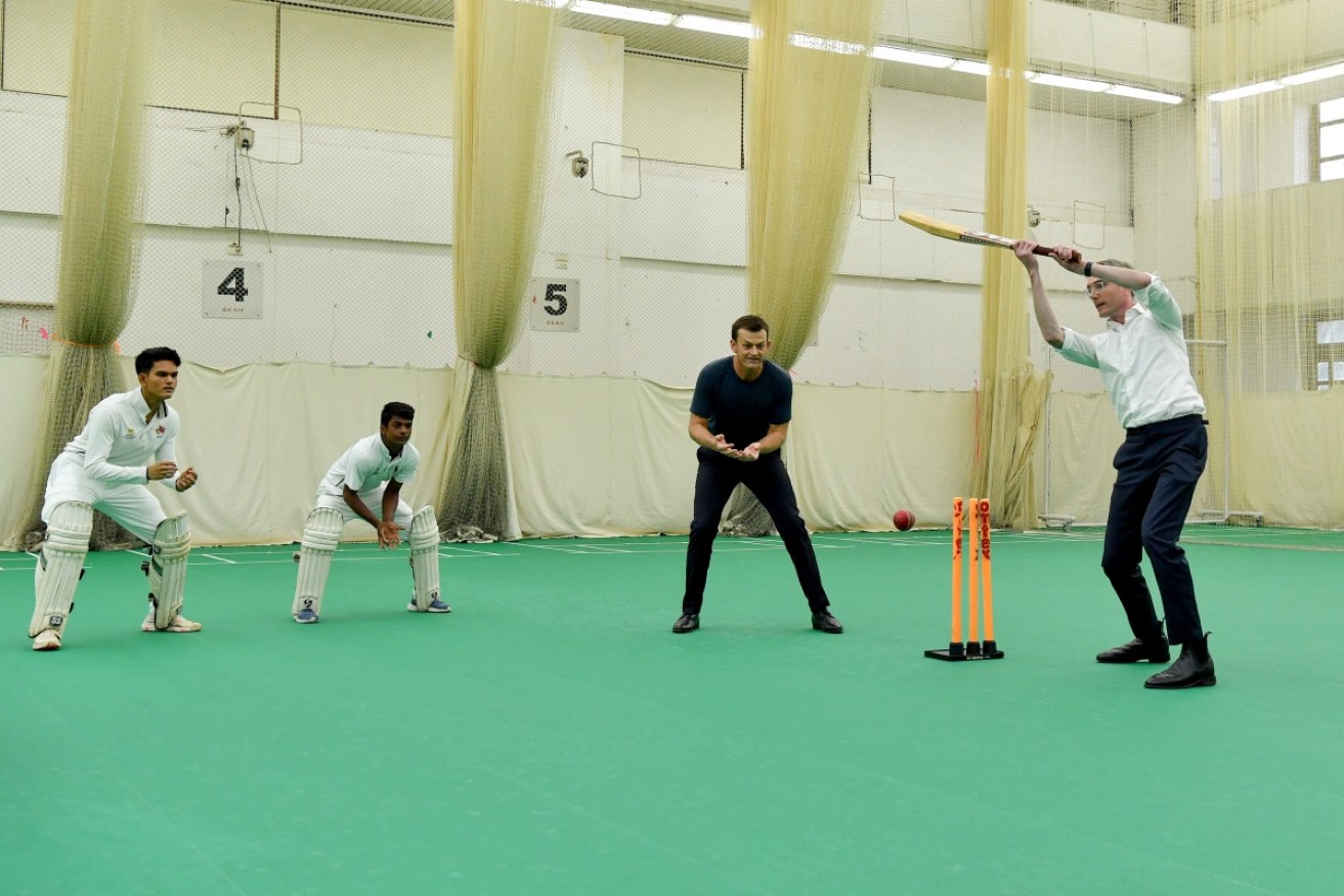NSW Premier Dominic Perrottet wields a bat as Adam Gilchrist and Mumbai under-19s players watch in India.