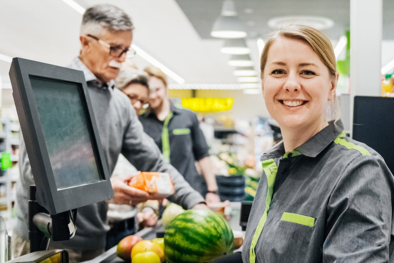 A portrait of a cashier smiling while working at the checkout at busy supermarket.