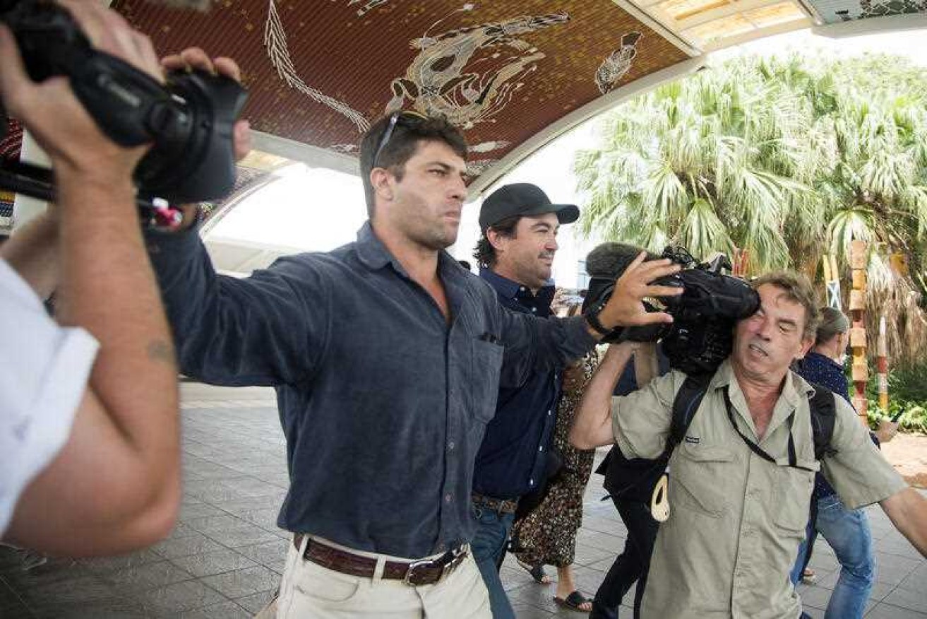 Minders jostle the media as Outback Wrangler star Matt Wright [centre] arrives at Darwin airport.