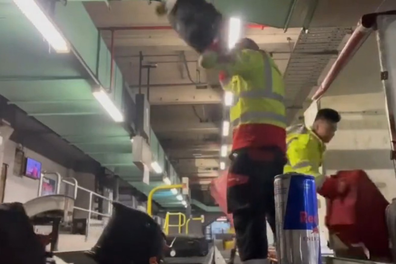 A baggager handler slams down a suitcase from above his head. 