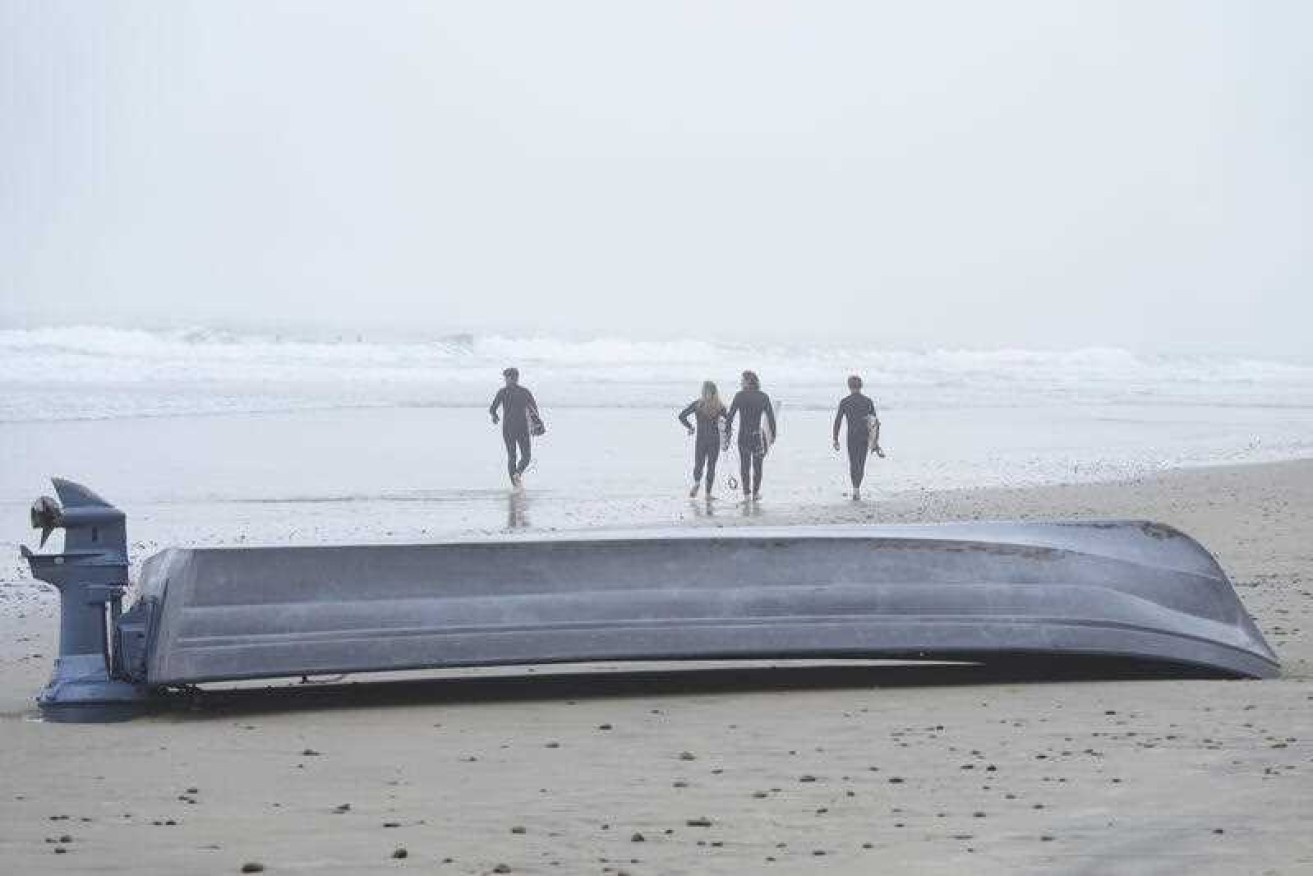 Surfers pass the overturned boat sitting on Blacks Beach.