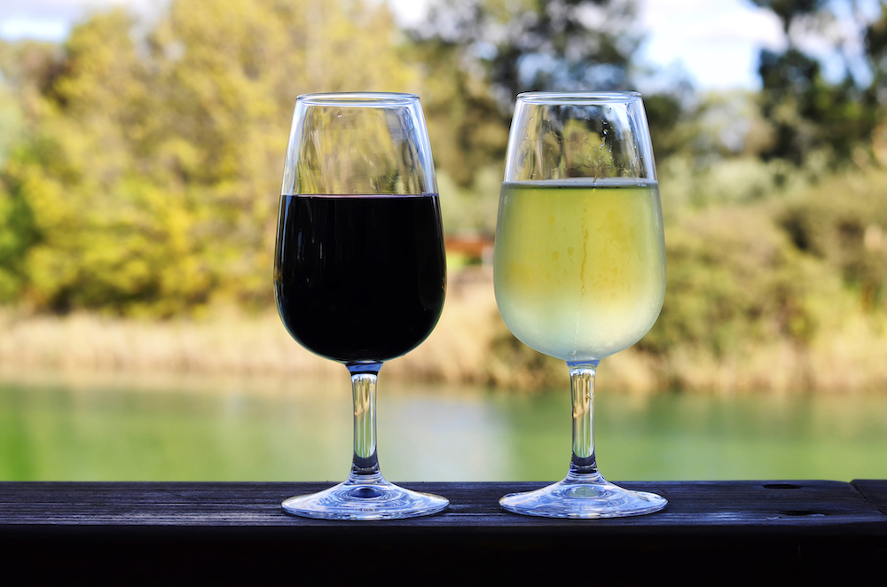 Two glasses of red and white wine on wooden rail overlooking Australian country setting.