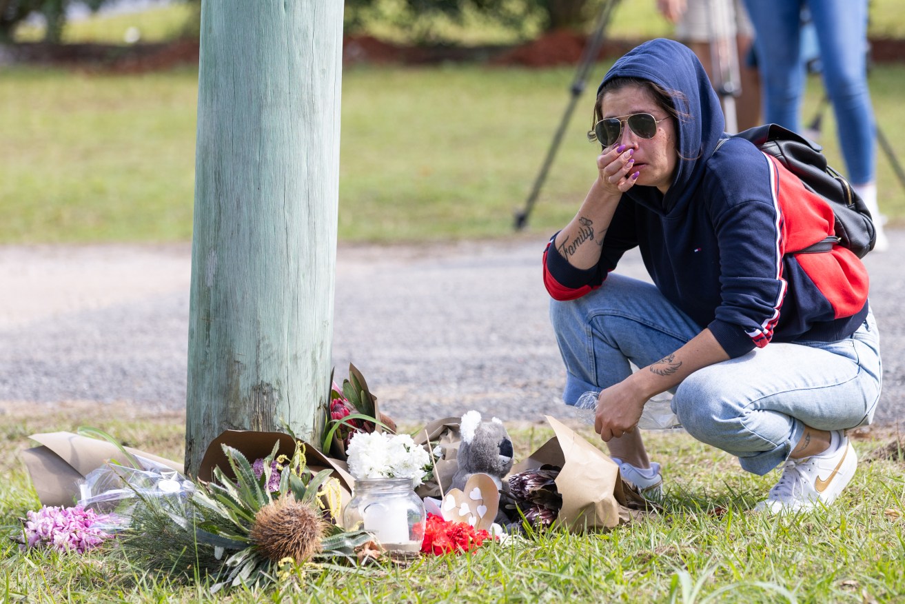 A mourner leaves tributes at the scene of a house fire that killed six people in Queensland.