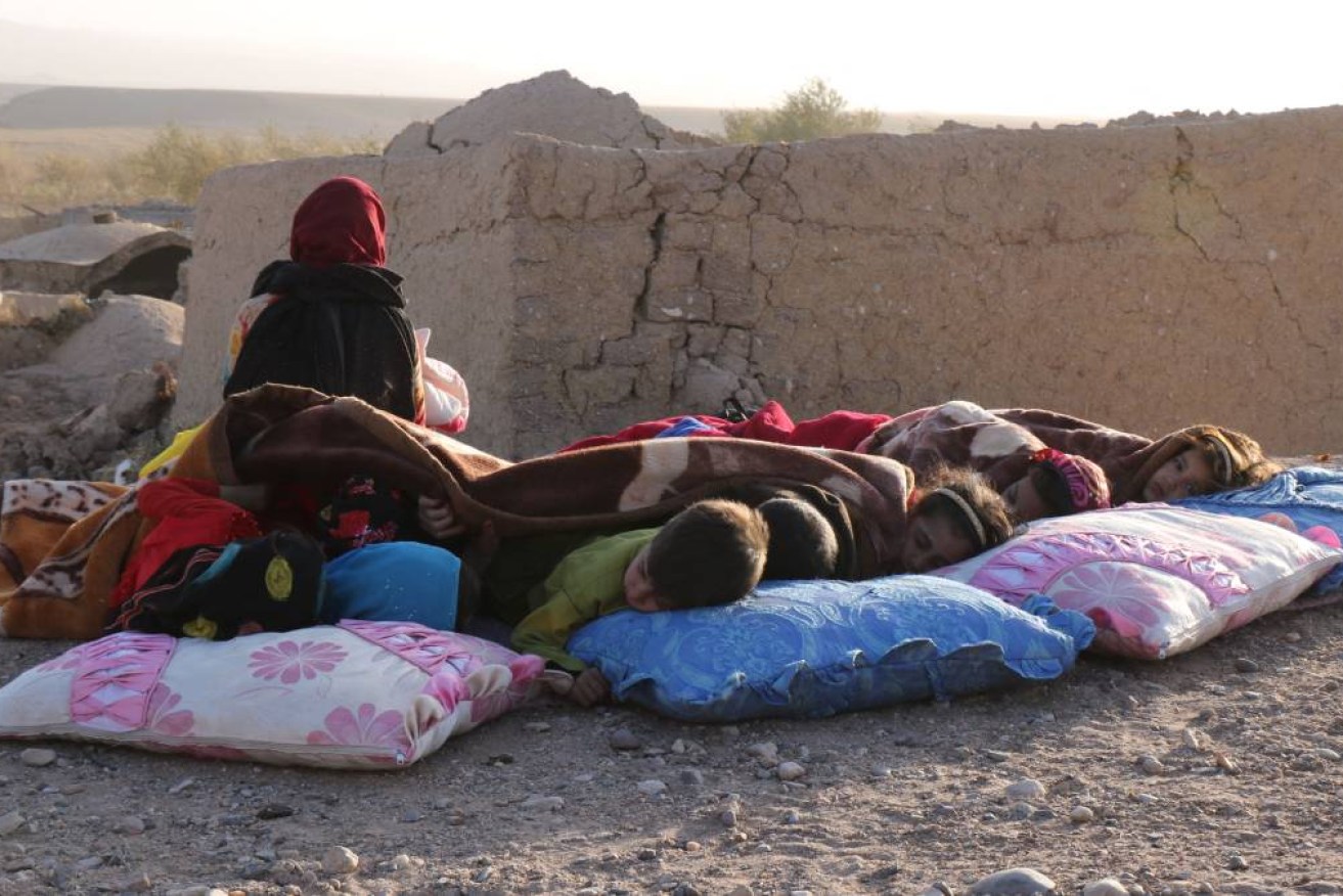 Afghan children rest under a blanket beside damaged houses after earthquake in Sarbuland village of Zendeh Jan district of Herat province.