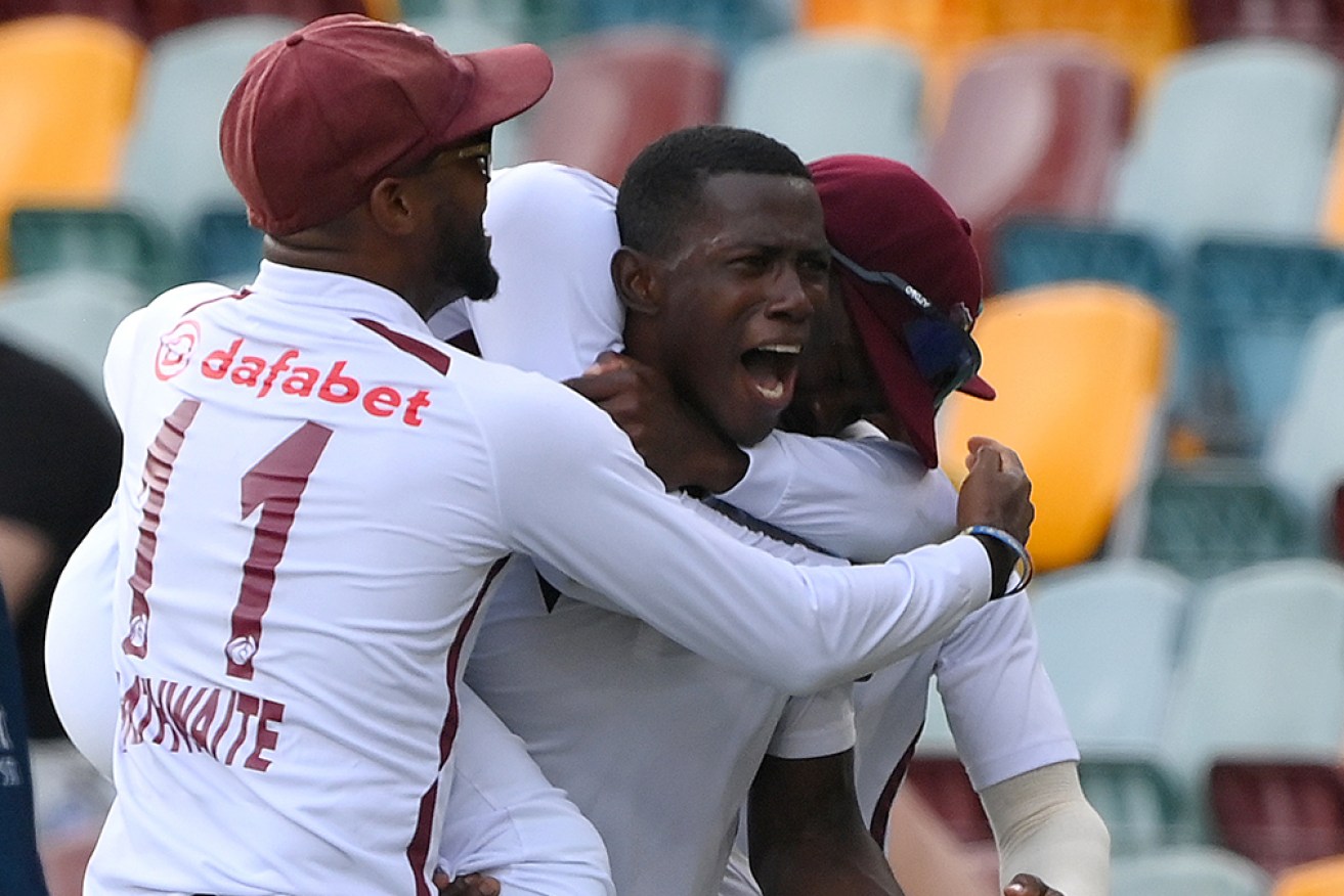 Teammates mob Shamar Joseph as the West Indies celebrate victory in Brisbane on Sunday. 