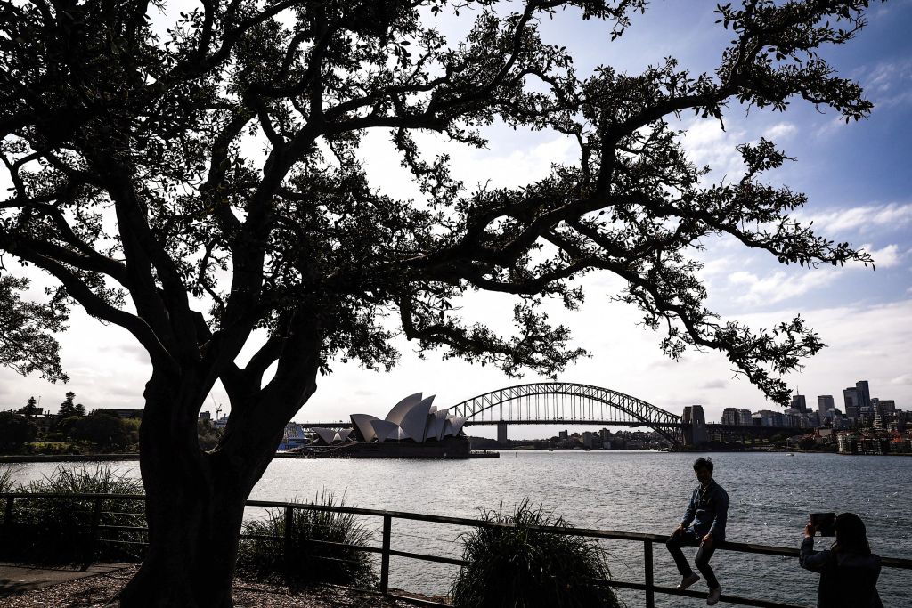 A tourists sits on a fence as he has his photograph taken in front of the Sydney Opera House and Sydney Harbour Bridge on a spring day on November 13, 2023. (Photo by DAVID GRAY / AFP) (Photo by DAVID GRAY/AFP via Getty Images)