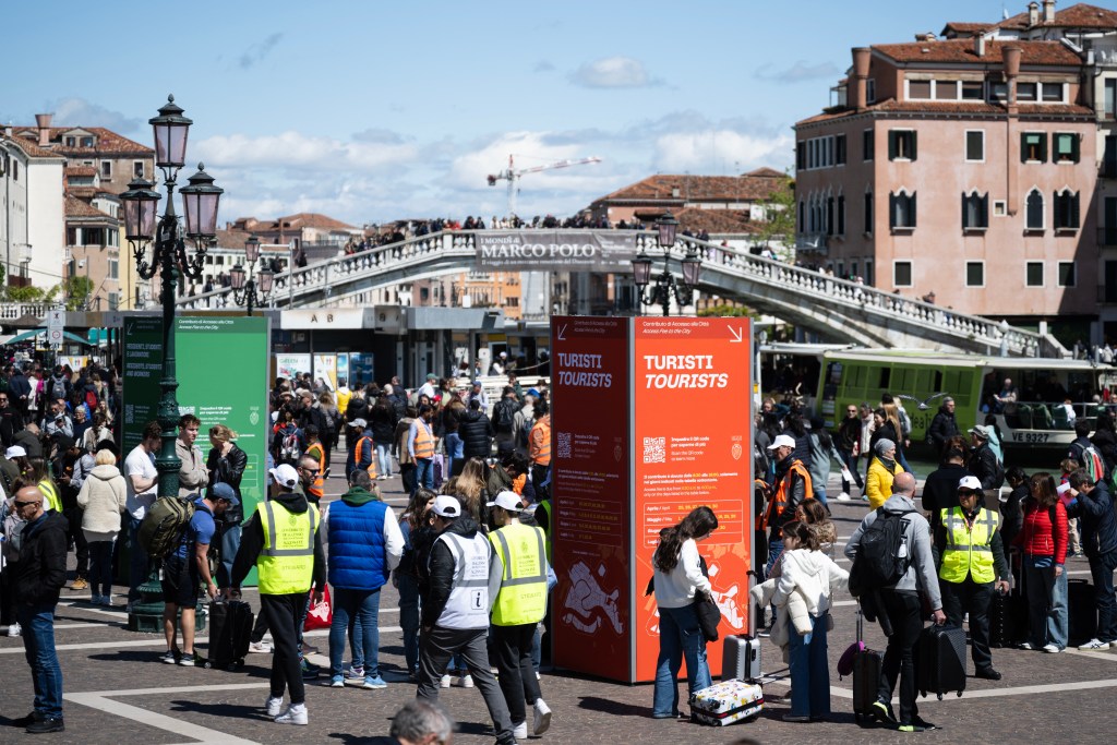 Tourists stand as they wait to pass controls and buy tickets in front of Santa Lucia train station in Venice on April 25, 2024. The new strategy to lower the number of tourists visiting the UNESCO World Heritage site calls for day-trippers to pay a five-euro ticket to enter the historic city centre and is due to start on April 25. 
